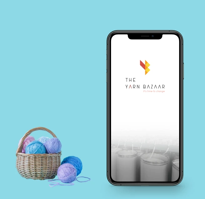 The Yarn Bazaar app splash screen on a phone beside a basket of yarn