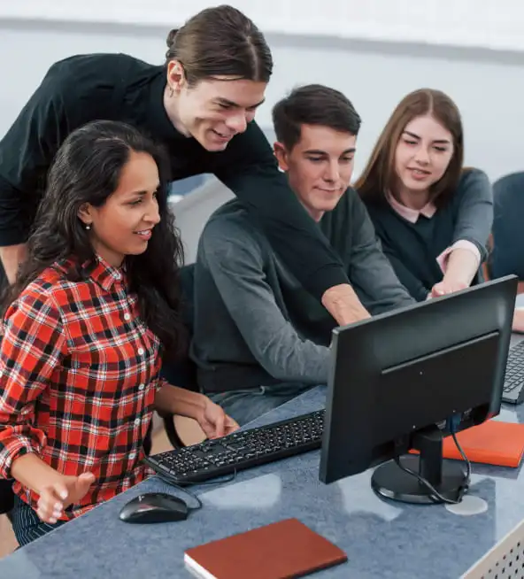 Four students gathered around a desktop computer, one pointing at the screen