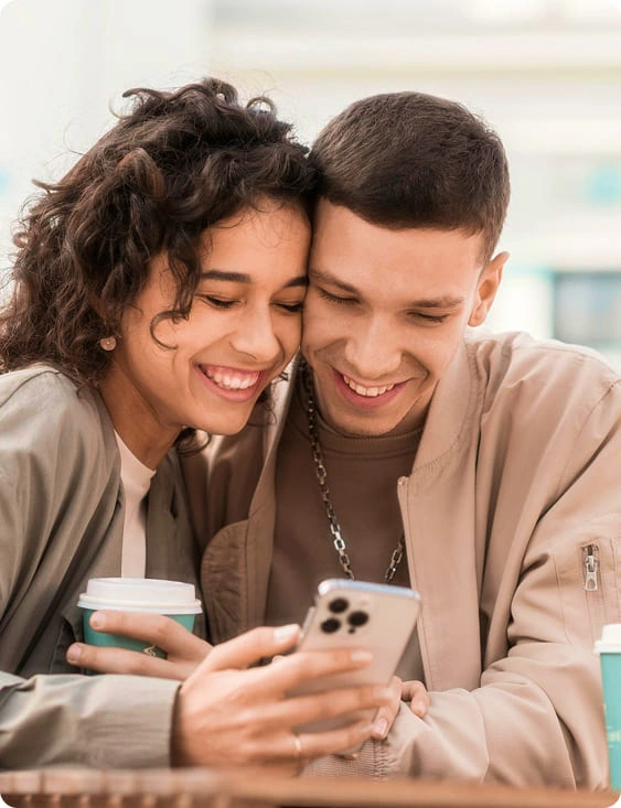 A smiling couple looking at a phone together over coffee