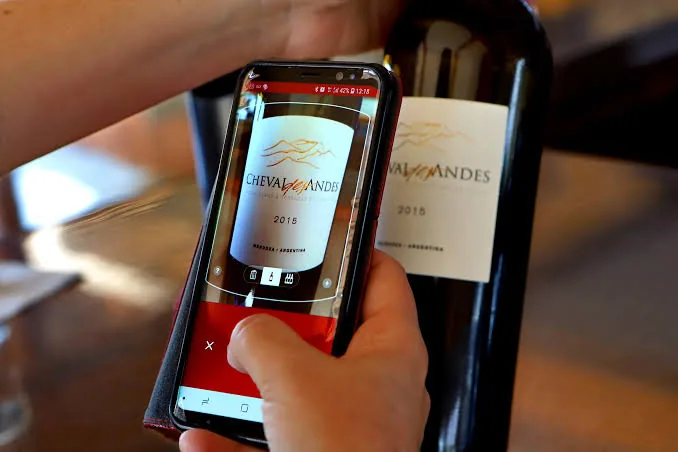 A hand holding a phone, scanning the label of a Cheval des Andes 2015 bottle with the Vivino app