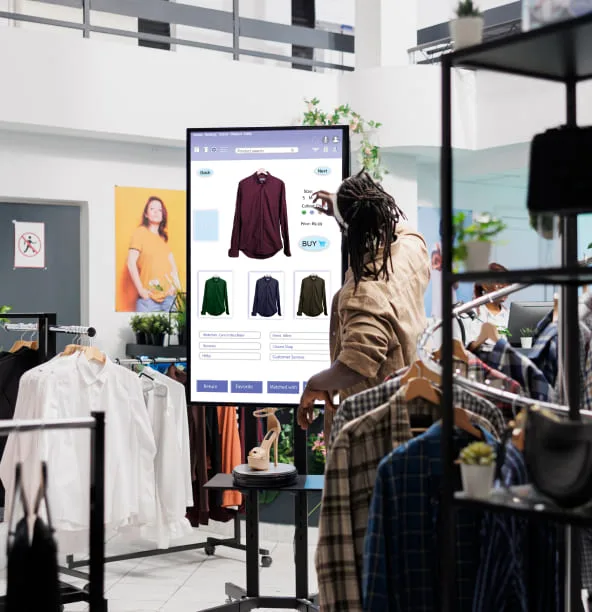 A shopper using a large touchscreen kiosk to browse shirts in a clothing store